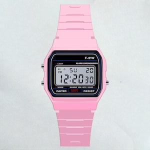 May include: A pink digital watch with a black rectangular face. The watch displays the time as 12:20:30, with the day and date visible. The watch band and case are a solid pink color, and the watch has the text "F-91W" on the top.
