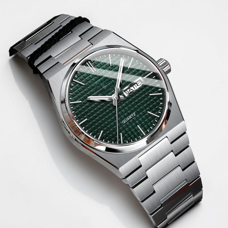 May include: A silver-toned wristwatch with a green textured dial. The watch features a rectangular face with the day of the week displayed. The watchband is made of silver-toned metal links. The word "QUARTZ" is printed on the watch face.