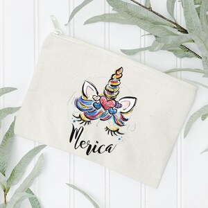 May include: A white canvas zippered pouch with a colourful unicorn illustration and the word "Merica" printed on it.