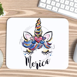 May include: A white mouse mat featuring a colourful unicorn illustration and the word "Merica" in black lettering. The unicorn has a blue, red and white mane and tail, and a gold horn. The unicorn is wearing a red, white and blue heart.
