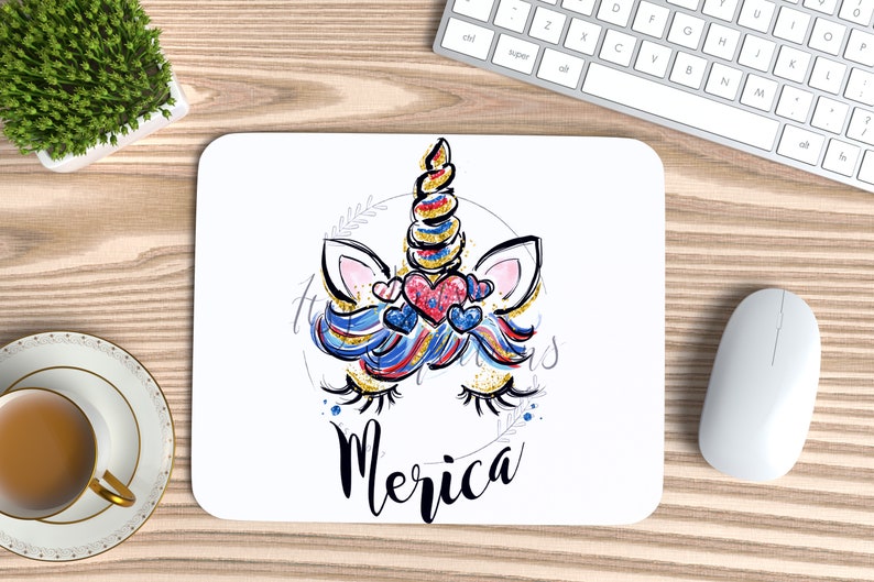 May include: A white mouse mat featuring a colourful unicorn illustration and the word "Merica" in black lettering. The unicorn has a blue, red and white mane and tail, and a gold horn. The unicorn is wearing a red, white and blue heart.