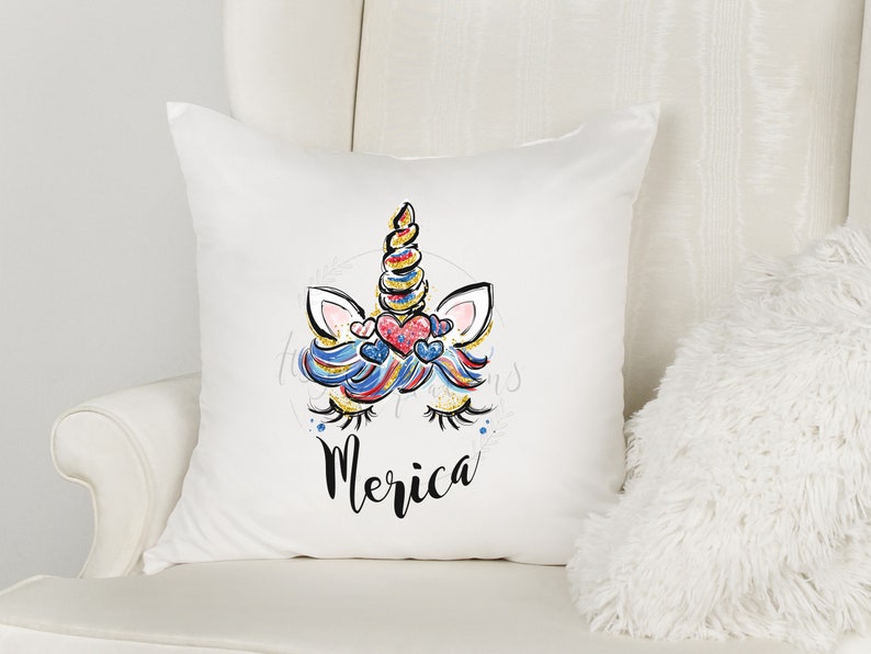 May include: White cushion featuring a colourful unicorn illustration and the word "Merica" printed on it.