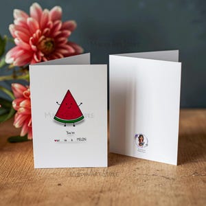 Può includere: Un biglietto d'auguri bianco con l'illustrazione di una fetta di anguria con un volto sorridente, braccia e gambe. Sotto l'illustrazione, il testo recita: You're one in a MELON, con una piccola icona a forma di cuore rosso. Il biglietto è aperto.