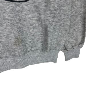 May include: A heather gray sweatshirt with a ribbed hem and cuffs. The fabric has a slightly textured appearance. There is a stain on the front of the sweatshirt. The bottom of the sweatshirt is visible.