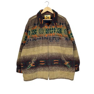 May include: A vintage brown jacket with a full zipper closure and two front pockets. The jacket features a geometric pattern in shades of orange, green, and brown. The jacket is hanging on a wooden hanger.