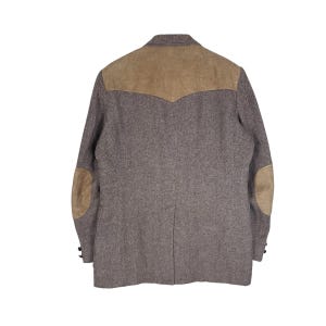 May include: A brown herringbone blazer featuring a tan suede yoke across the upper back and matching tan suede elbow patches on each sleeve. The jacket includes a notched collar, a single back vent, and small dark buttons at the sleeve cuffs.