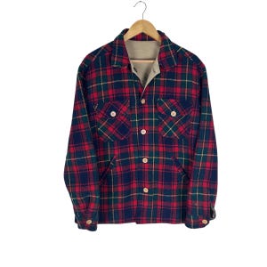 May include: A long-sleeve button-up shirt featuring a red, navy blue, and yellow plaid pattern. The shirt includes a pointed collar, two chest pockets with buttoned flaps, and light-colored buttons down the front placket and on the cuffs.