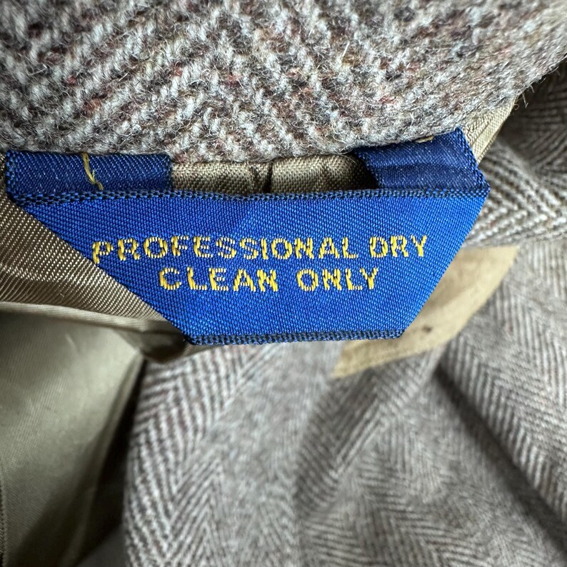 May include: A brown and white herringbone patterned fabric garment featuring a blue rectangular clothing label with the yellow text PROFESSIONAL DRY CLEAN ONLY stitched into the interior lining of the piece.