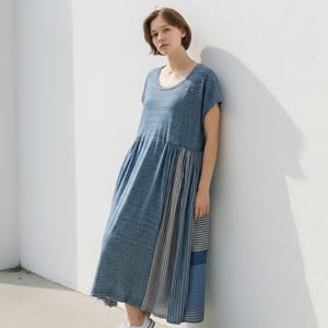 Può includere: Abito a righe blu e bianche con scollo tondo e maniche corte. L'abito presenta una vita arricciata e una gonna fluida con righe verticali nelle tonalità del blu e del grigio. La modella indossa scarpe da ginnastica bianche.