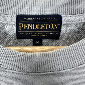 Puede incluir: Primer plano de una sudadera gris con cuello redondo acanalado. La etiqueta negra dice "WARRANTED TO BE A PENDLETON PENDLETON WOOLEN MILLS SINCE 1863" en letras doradas. La talla "M" est&aacute; impresa debajo.