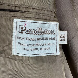 May include: A white rectangular clothing label sewn onto a brown quilted fabric lining. The label features the text Pendleton, HIGH GRADE WESTERN WEAR, PENDLETON WOOLEN MILLS, PORTLAND, OREGON. A smaller attached tag displays the size 44 LONG.