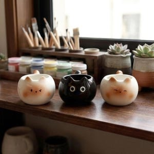 Op de afbeelding: Een witte keramische mok met een zwart handvat en de tekst "But First, Coffee" in een vetgedrukte, zwarte letter. De mok staat tegen een vage achtergrond, wat een gezellige setting suggereert.