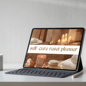 Op de afbeelding: Een tablet met een "self-care reset planner" met een kaars, roos en crème pot. De tablet staat op een toetsenbordhoes met een stylus. De achtergrond toont kaarsen en handdoeken, wat een ontspannen thema creëert.