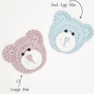 May include: Two crochet bear head appliques. One is Graige Pink with a white muzzle and black eyes, the other is Duck Egg Blue with a white muzzle and black eyes. Both feature stitched noses and rounded ears, with text labels pointing to each.