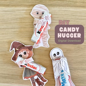 May include: Three paper cutouts featuring a mummy, a witch, and a ghost, each holding a Kinder chocolate bar. The text DIY CANDY HUGGER Digital Download is printed in a dark rectangle. The characters have illustrated arms that wrap around the candy.