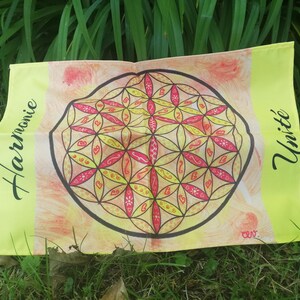Puede incluir: Un textil rectangular amarillo con un diseño geométrico central en rojo, amarillo y negro. El diseño está rodeado por un contorno negro. Las palabras "Harmonie" y "Unité" están escritas en los lados.