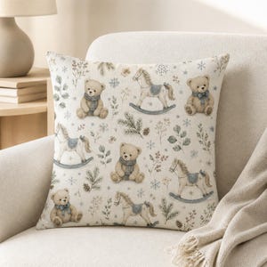 May include: A square throw pillow featuring a repeating pattern of light brown teddy bears wearing blue scarves, rocking horses with blue saddles, pine branches, and snowflakes on a cream-coloured fabric background.