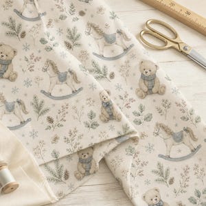 May include: A cream-coloured fabric featuring a repeating pattern of brown teddy bears wearing blue scarves, light brown rocking horses with blue saddles, pine branches, pinecones, and snowflakes. A wooden ruler and gold scissors are visible.