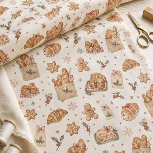 May include: A cream-colored fabric featuring a repeating pattern of brown gingerbread men, star-shaped cookies, croissants, baguettes in paper bags, holly sprigs, and snowflakes. The textile is displayed with a pair of gold scissors and thread spools.