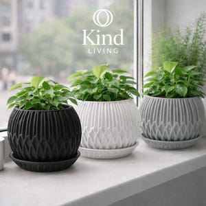 Puede incluir: Tres macetas decorativas con plantas verdes sobre un alféizar. Las macetas son negras, blancas y grises, cada una con un diseño texturizado único. El texto "Kind LIVING" es visible en el fondo.