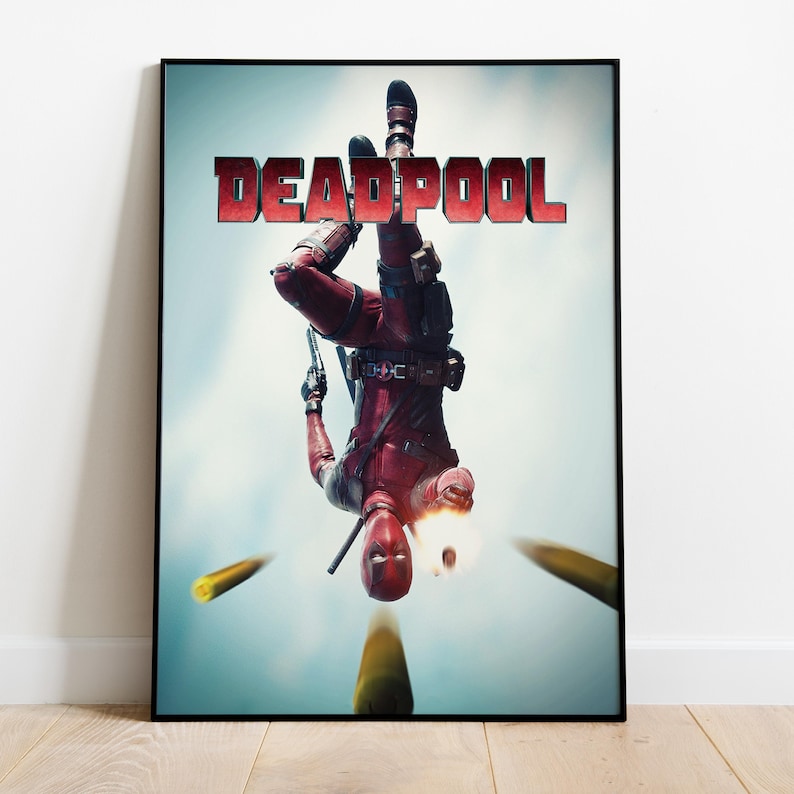 May include: A framed poster featuring the character Deadpool in a red and black suit, holding a gun and falling upside down. The word "DEADPOOL" is displayed in red block letters at the top. Yellow bullets are shown in motion.