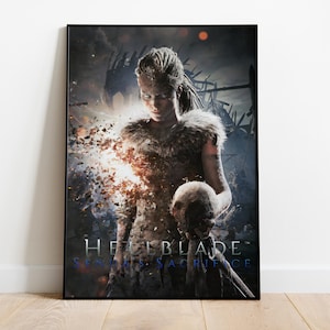 Puede incluir: Un póster enmarcado que presenta a una mujer con cabello trenzado, vestida con una prenda con ribete de piel, sosteniendo una calavera. El póster tiene una estética oscura y dramática con el título "Hellblade: Senua's Sacrifice" en azul y blanco.