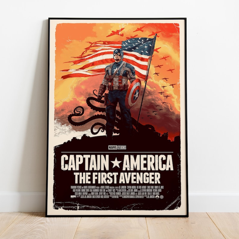 May include: A framed poster for "Captain America: The First Avenger." The artwork features Captain America standing on a rocky outcrop, holding a shield and the American flag. The background is an orange and red sky with silhouettes of planes.