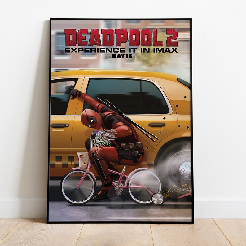 May include: A framed poster for the movie Deadpool 2. The poster features Deadpool riding a pink bicycle next to a yellow taxi cab. The poster's title is in red letters, with the tagline "Experience it in IMAX" and the date "May 18".
