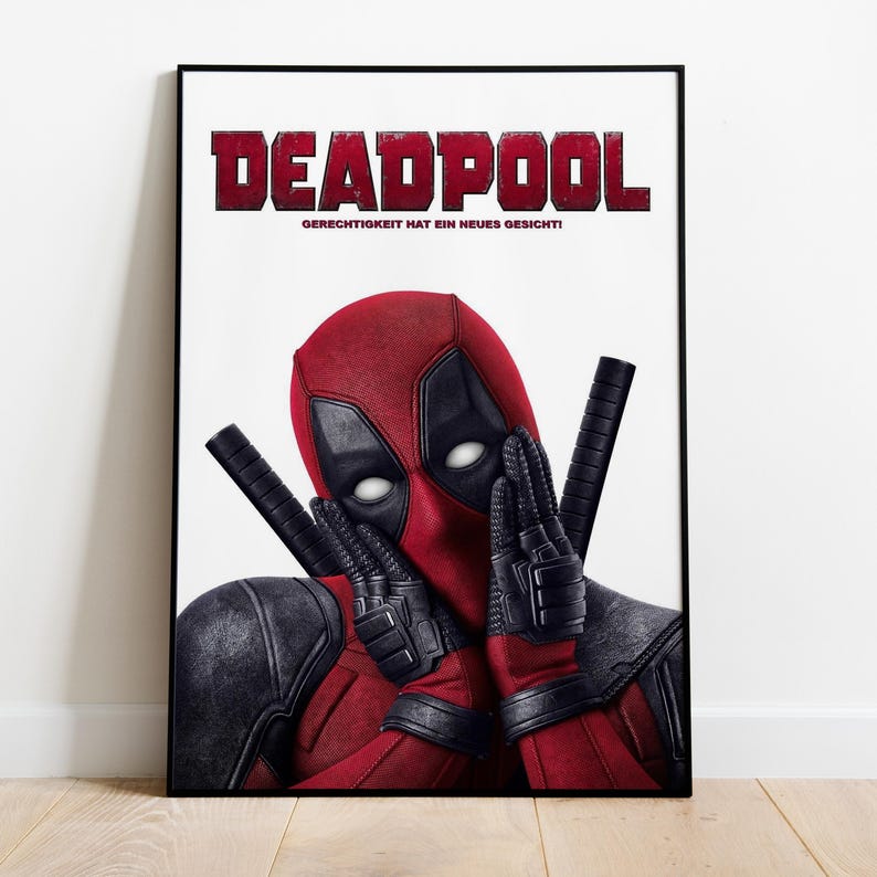 May include: A framed poster featuring the character Deadpool. The poster has a white background with the word "DEADPOOL" in red block letters at the top. The character is wearing a red and black costume and making a peace sign with his hands.