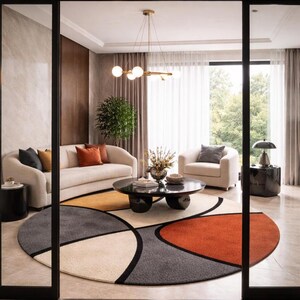 May include: A modern living room with a cream-colored sofa, armchair, and a round coffee table. A colorful, geometric rug in shades of gray, orange, and cream sits in the center of the room. A gold chandelier hangs above the coffee table.