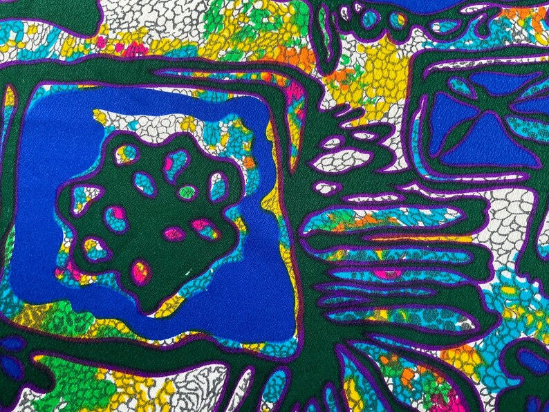 Puede incluir: Tela de patr&oacute;n abstracto con fondo verde, contornos azules y morados y un patr&oacute;n floral blanco, amarillo y verde.