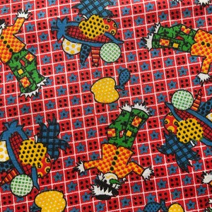 May include: A red fabric featuring a repeating grid pattern with small blue flowers. The print includes scarecrows wearing yellow polka-dot shirts and green pants, alongside yellow apples and blue corn cobs with yellow and green dotted textures.