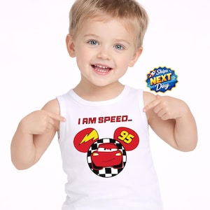 A young boy wearing a white tank top with a cartoon character and the text "I AM SPEED 95" is smiling and pointing to a sticker with the text "Shops NEXT DAY".