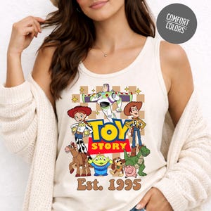 A woman wearing a white tank top with a graphic of characters from the Toy Story movie, posing against a white background.