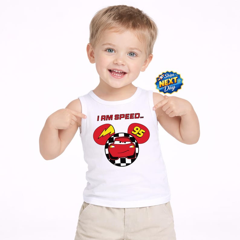 A young boy wearing a white tank top with a cartoon character and the text "I AM SPEED 95" is smiling and pointing to a sticker with the text "Shops NEXT DAY".