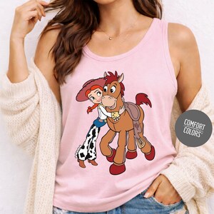 A woman wearing a pink tank top with a cartoon image of a girl hugging a horse.