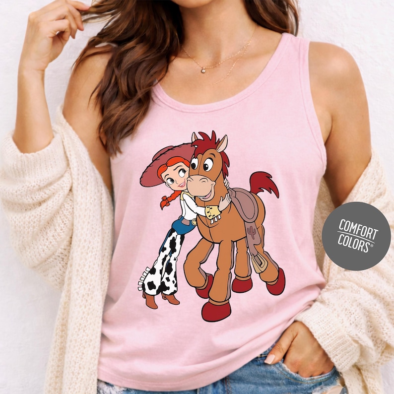 A woman wearing a pink tank top with a cartoon image of a girl hugging a horse.
