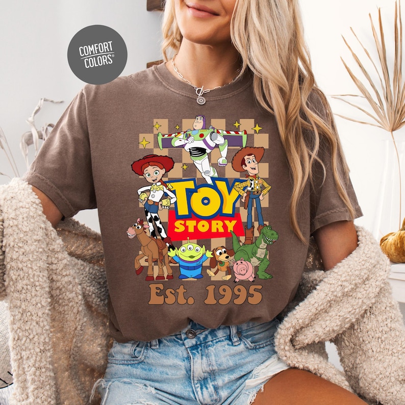 A woman wearing a brown t-shirt with a graphic of characters from the Toy Story movie, including Buzz Lightyear, Woody, and other beloved characters.