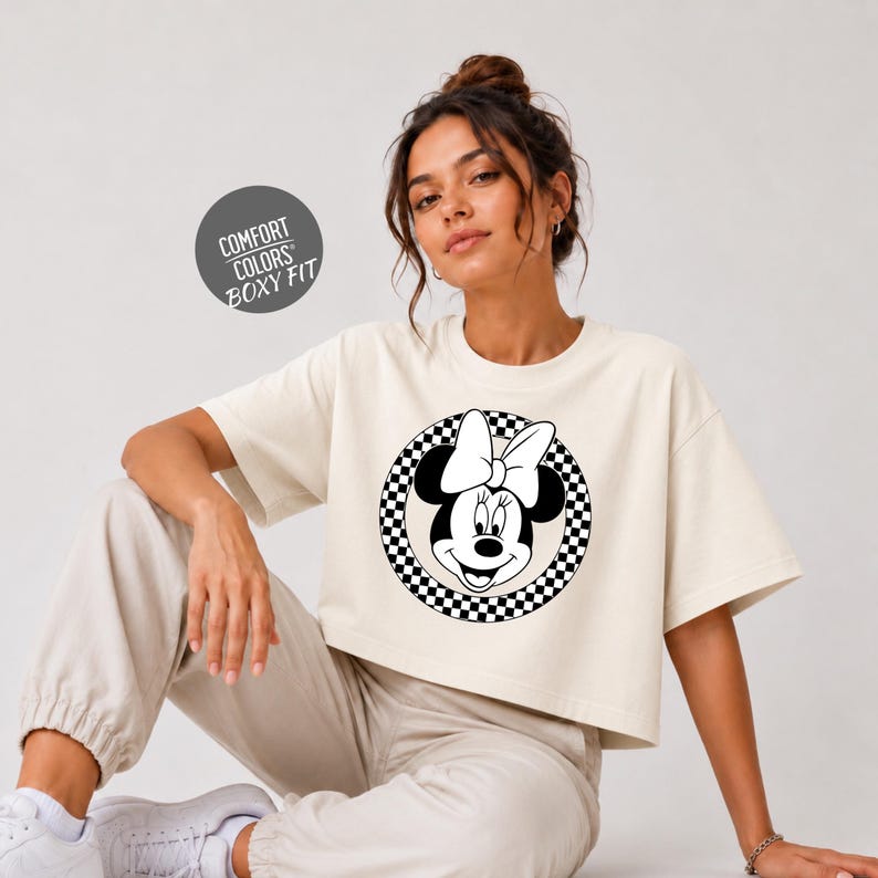 A woman wearing a white t-shirt with a Minnie Mouse graphic and a black and white checkered pattern, posing against a plain background.