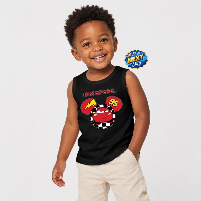 A young boy with curly hair is smiling and wearing a black tank top with a graphic of a lightning bolt and a character from the Disney movie Cars.