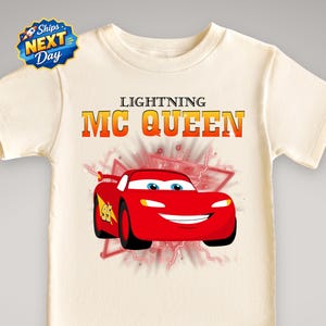 A white t-shirt with a graphic design featuring a red car with the character Lightning McQueen on it.