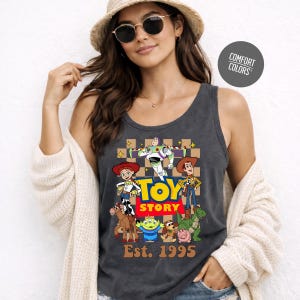 A woman wearing a gray tank top with a graphic of characters from the Toy Story movie, including Buzz Lightyear, Woody, and other beloved characters. She is also wearing a hat and sunglasses.