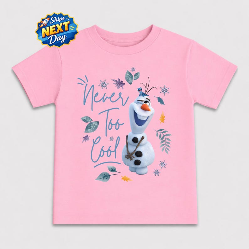 A pink t-shirt with a graphic design featuring the character Olaf from the Disney movie Frozen. The design includes Olaf holding a snowman and the text "Never Too Cool" written above him.