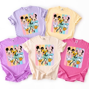 a collection of five t-shirts featuring the Disney characters Mickey Mouse, Minnie Mouse, Donald Duck, Goofy, and Daisy Duck.