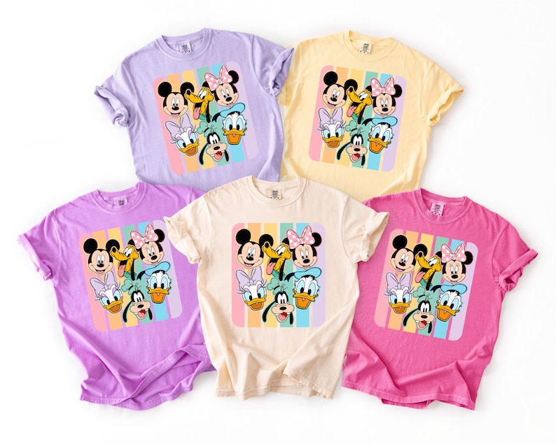 a collection of five t-shirts featuring the Disney characters Mickey Mouse, Minnie Mouse, Donald Duck, Goofy, and Daisy Duck.