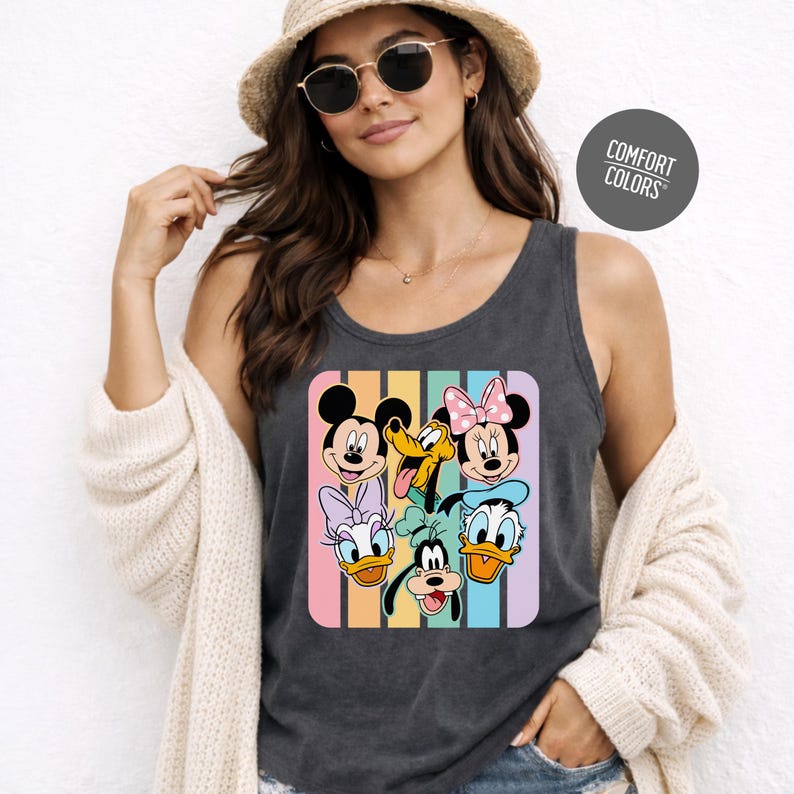 A woman wearing a hat and sunglasses, with a tank top featuring a graphic of Disney characters Mickey Mouse, Minnie Mouse, Donald Duck, Goofy, and Pluto.