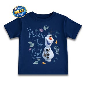 A navy blue t-shirt with a graphic design featuring a smiling snowman character and the text "Never Too Cool" written above it.