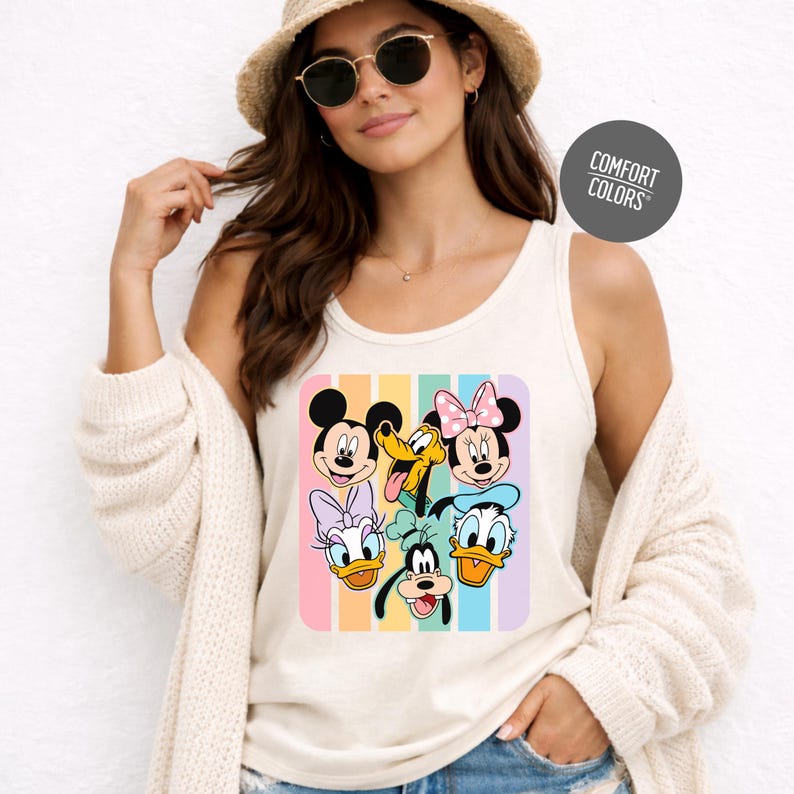 A woman wearing a white tank top with a colorful graphic of Disney characters, including Mickey Mouse, Minnie Mouse, Donald Duck, Goofy, and Pluto, posing against a white background.