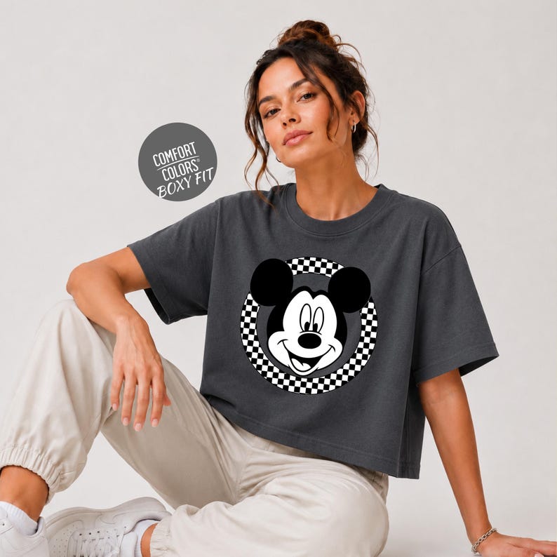 A woman wearing a gray crop top with a black and white Mickey Mouse graphic, posing against a white background.
