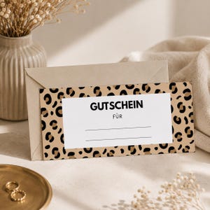Könnte beinhalten: Ein rechteckiger Gutschein mit einem beigefarbenen und schwarzen Leopardenmuster-Rand. Die Mitte ist weiß mit dem schwarzen Text GUTSCHEIN FÜR und zwei horizontalen Linien zum Beschriften. Der Gutschein steckt in einem hellbraunen Umschlag.